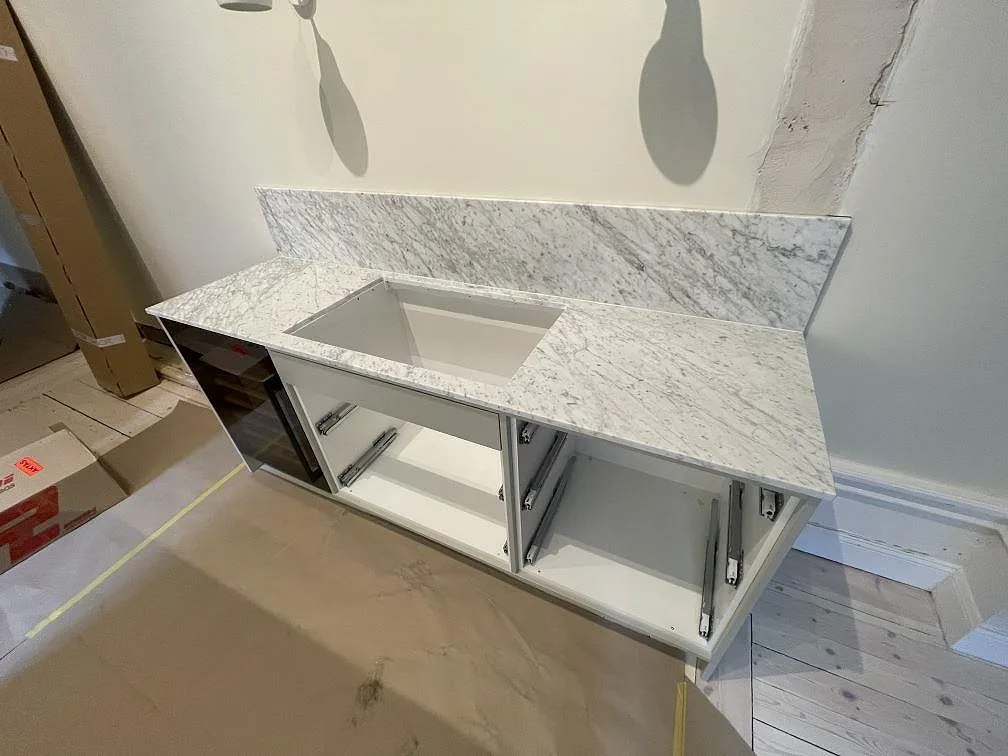 Köksbänk i matt Carrara C-marmor med uppvikt marmorstänkvägg och öppen diskhohåltagning under monteringen i ett kök i Stockholm.