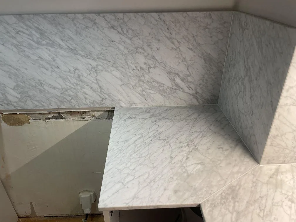 Köksbänkskiva i Carrara C marmor sedd uppifrån, matt finish med mjuk grå ådring och uppvikt stänkkant, i ett kök i Stockholm.