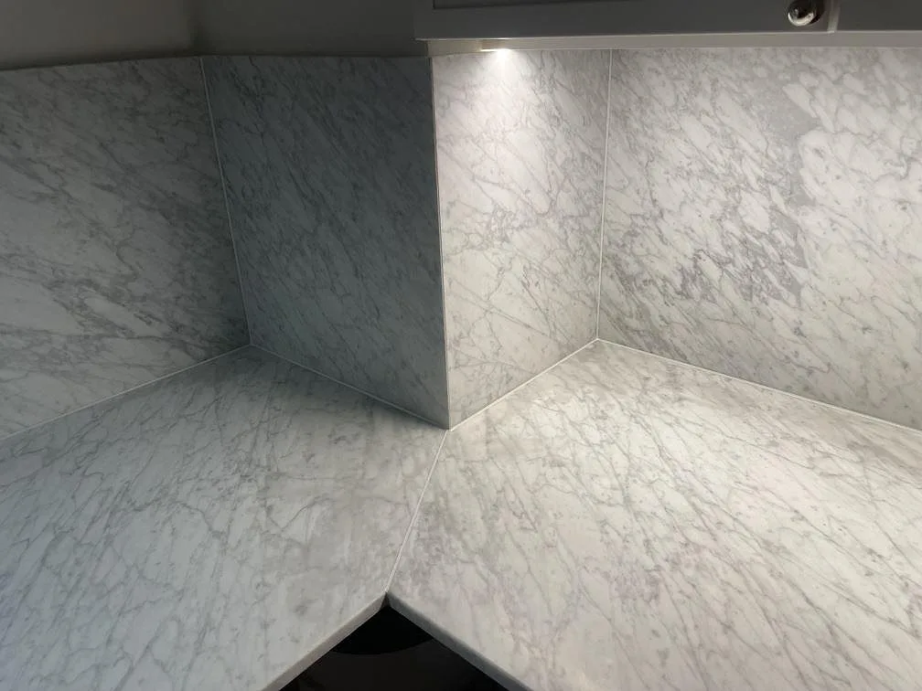 Närbild på matt Carrara C marmor i hörnet mellan bänkskiva och stänkskydd, med tydlig grå ådring, i ett kök i Stockholm.