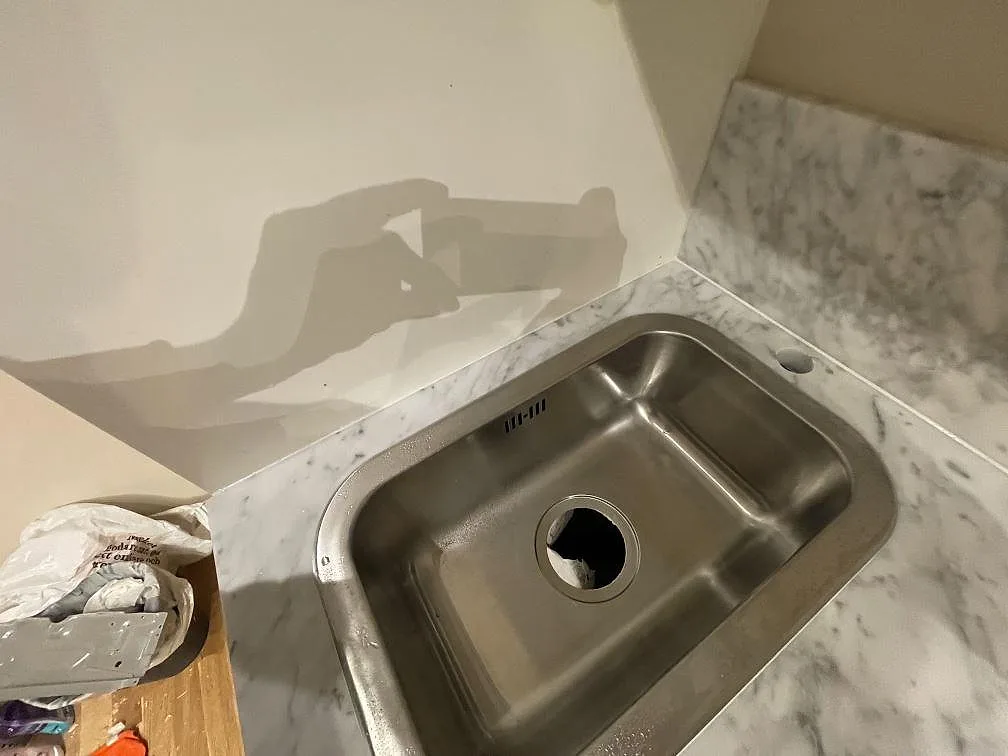 Underlimmad rostfri diskho i vit Carrara C marmorbänkskiva mot oklädd vägg i ett kök i Stockholm.