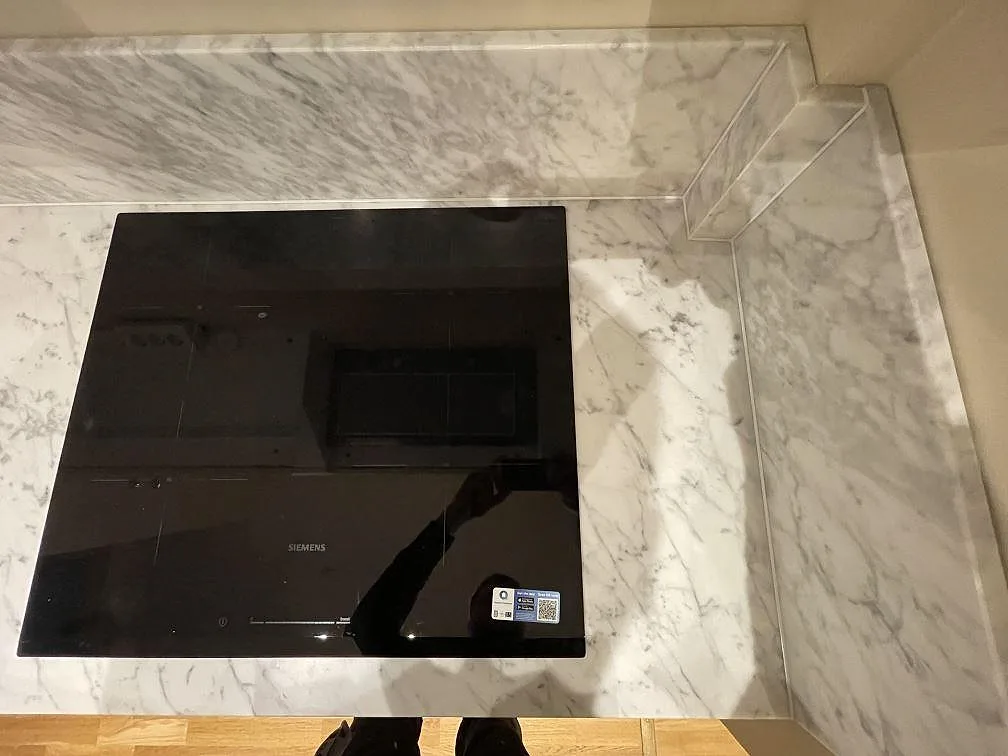 Svart infälld Siemens induktionshäll i matt Carrara C marmorbänkskiva med grå ådring i ett kök i Stockholm.