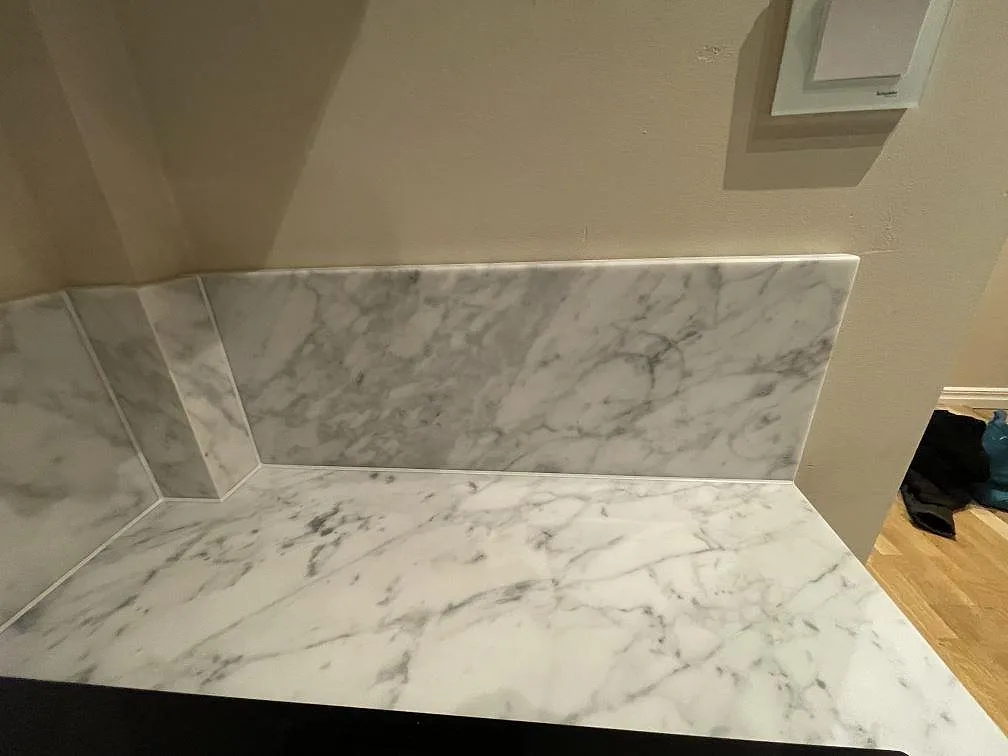 Låg uppvikt stänkkant i Carrara C marmor i hörnet av en matt marmorbänkskiva i ett kök i Stockholm.