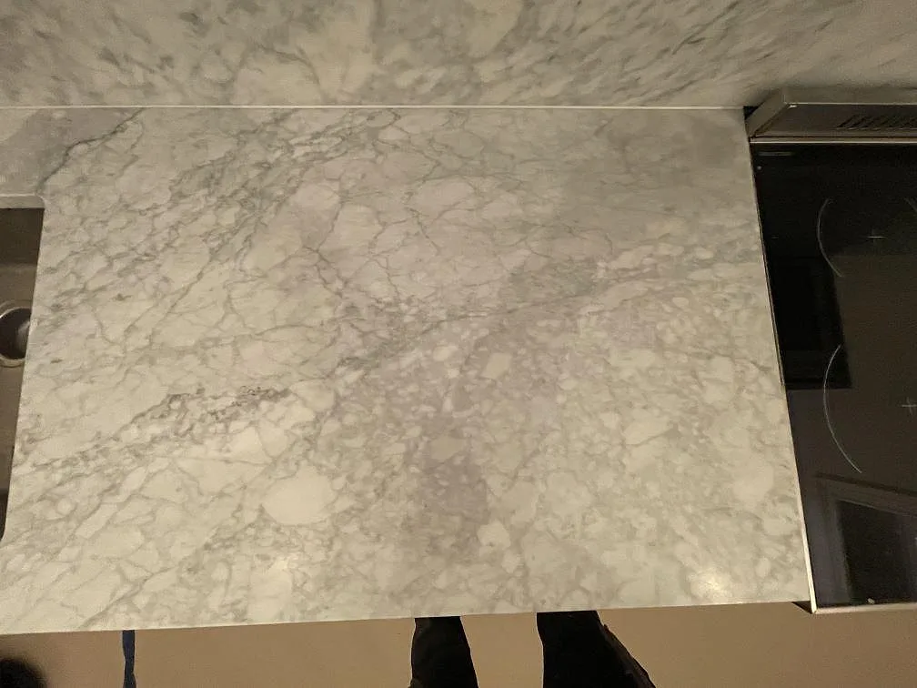 Närbild ovanifrån på den matta Carrara C-bänkskivan i köket, med tydlig grå marmorådring intill induktionshällen, i Stockholm.