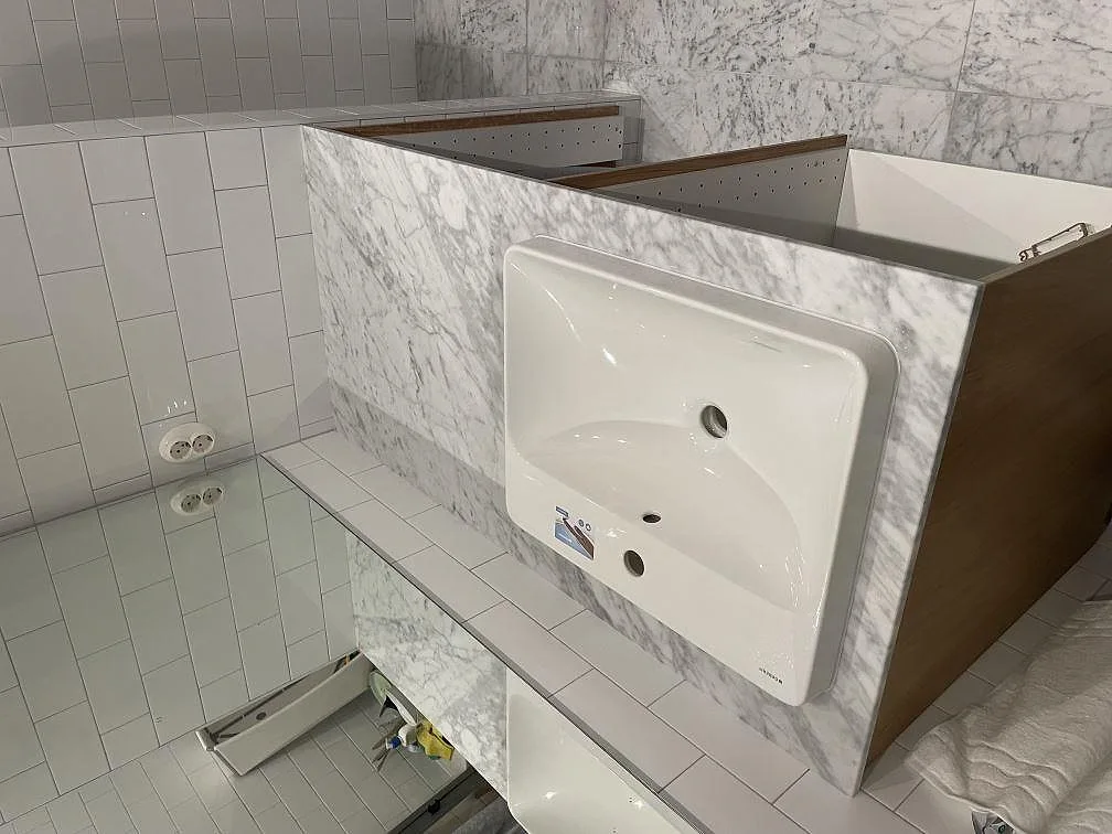 Tvättställsbänk i matt Carrara C-marmor med vitt porslinstvättställ och uppvikt marmorstänkskydd i ett badrum i Stockholm.