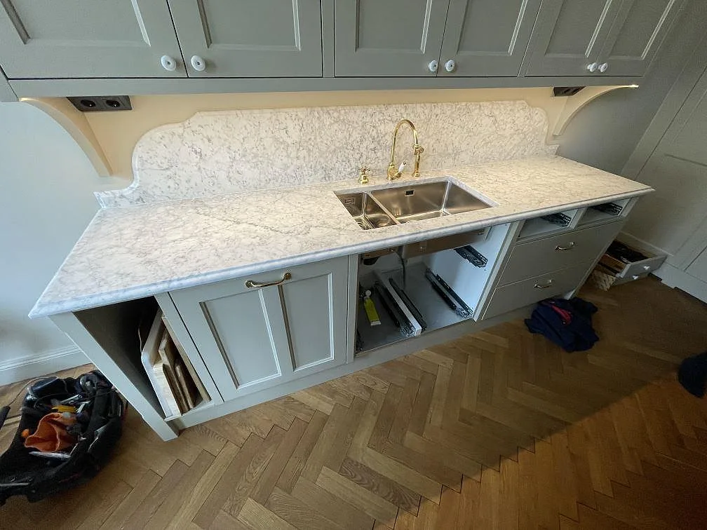 Underlimmad rostfri diskho och mässingsblandare i Carrara C marmorbänkskiva med formad marmorstänkskydd i ett kök i Stockholm.