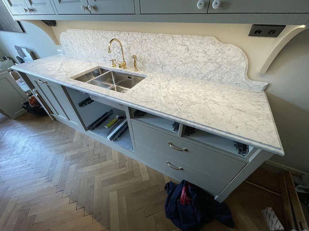Stänkskydd och bänkskiva i matt Carrara C marmor med underlimmad rostfri diskho och mässingsblandare i ett kök i Stockholm.