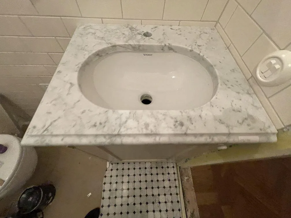 Bänkskiva i Carrara C marmor med underlimmat vitt tvättställ i ett badrum med mosaikgolv i Stockholm.