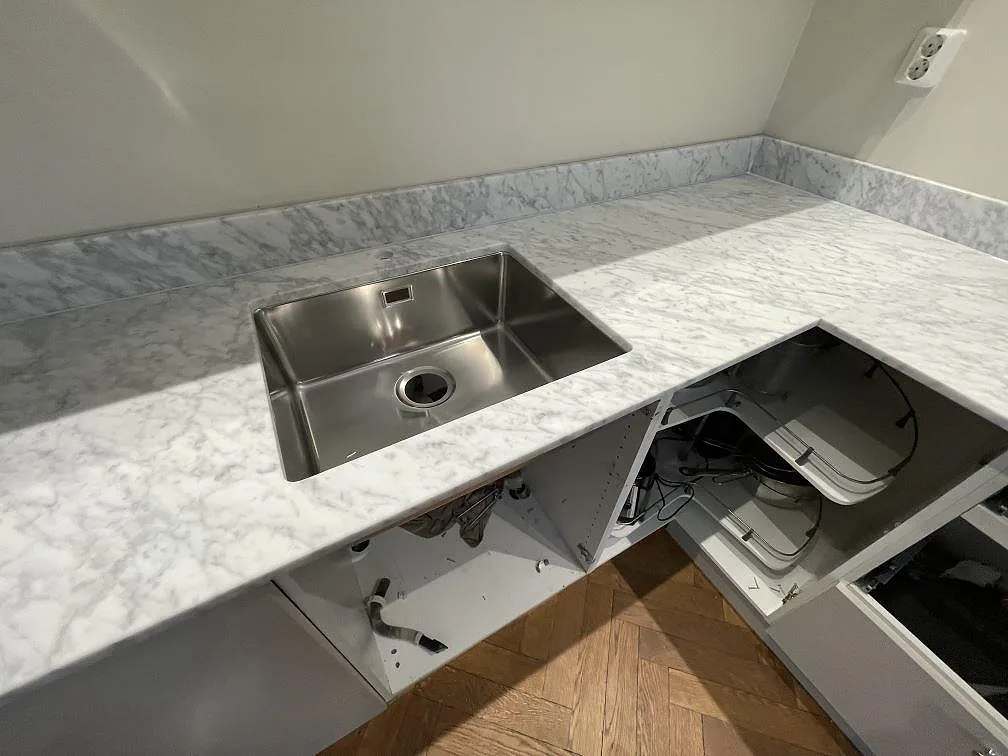 Underlimmad rostfri enkelho infälld i matt Carrara C-marmorbänk med diskret grå ådring i ett kök i Stockholm.