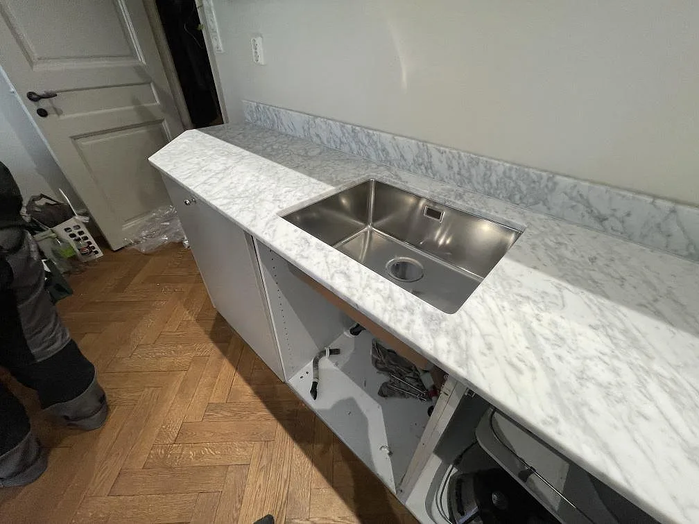 Köksbänk i Carrara C-marmor med underlimmad rostfri diskho och uppvikt stänkkant under montering i ett kök i Stockholm.
