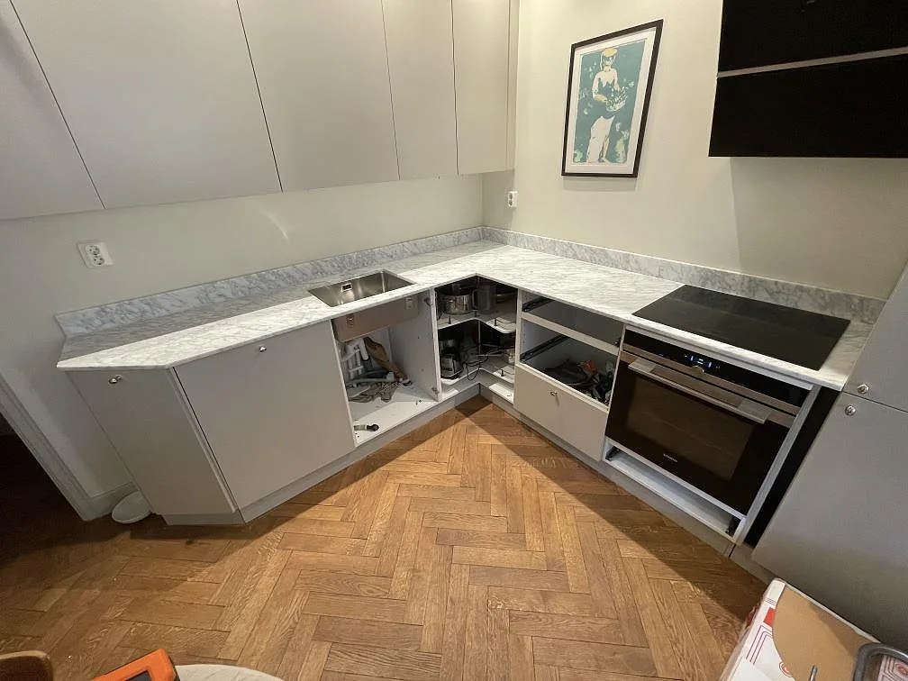 Översikt över L-format kök med matt Carrara C-marmorbänk, infälld induktionshäll och inbyggd ugn i Stockholm.