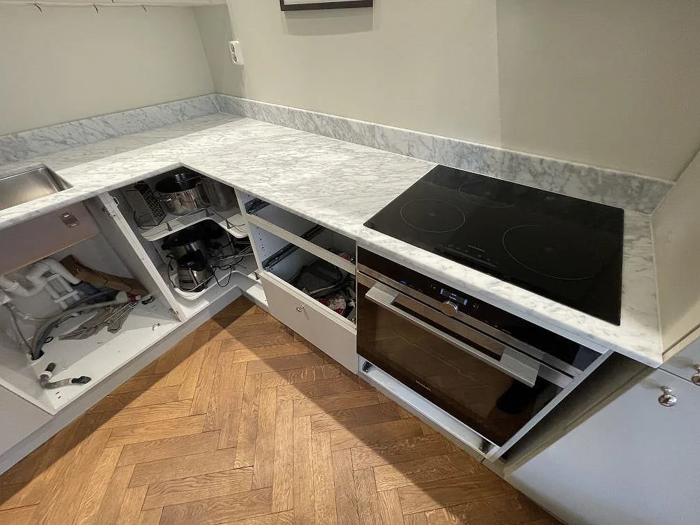 L-formad köksbänk i Carrara C-marmor med underlimmad rostfri diskho och infälld svart induktionshäll under montering i ett kök i Stockholm.