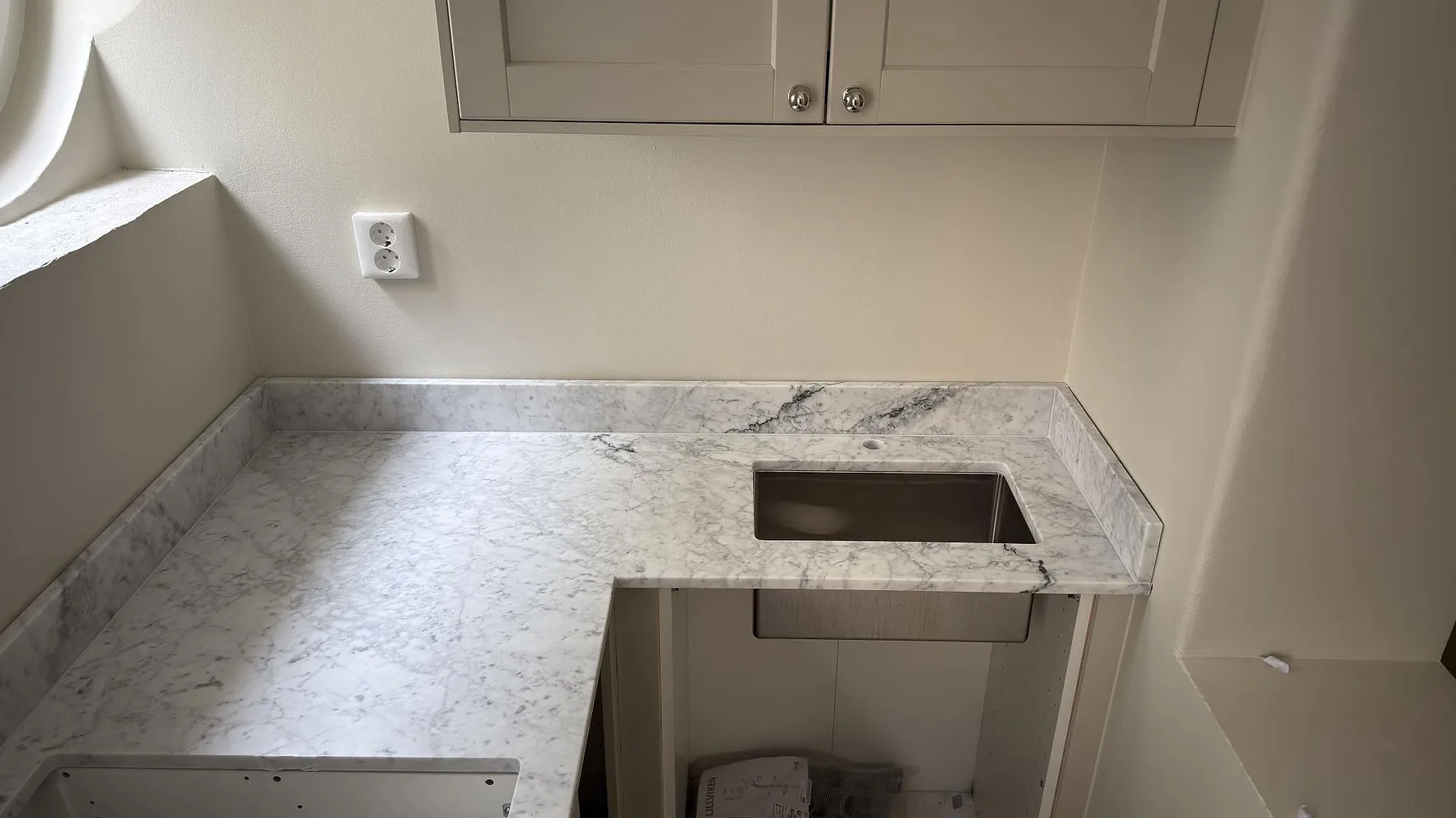 Underlimmad rostfri diskho monterad under matt Carrara C marmorbänkskiva i ett kök i Stockholm, med tydlig mörkgrå ådring.