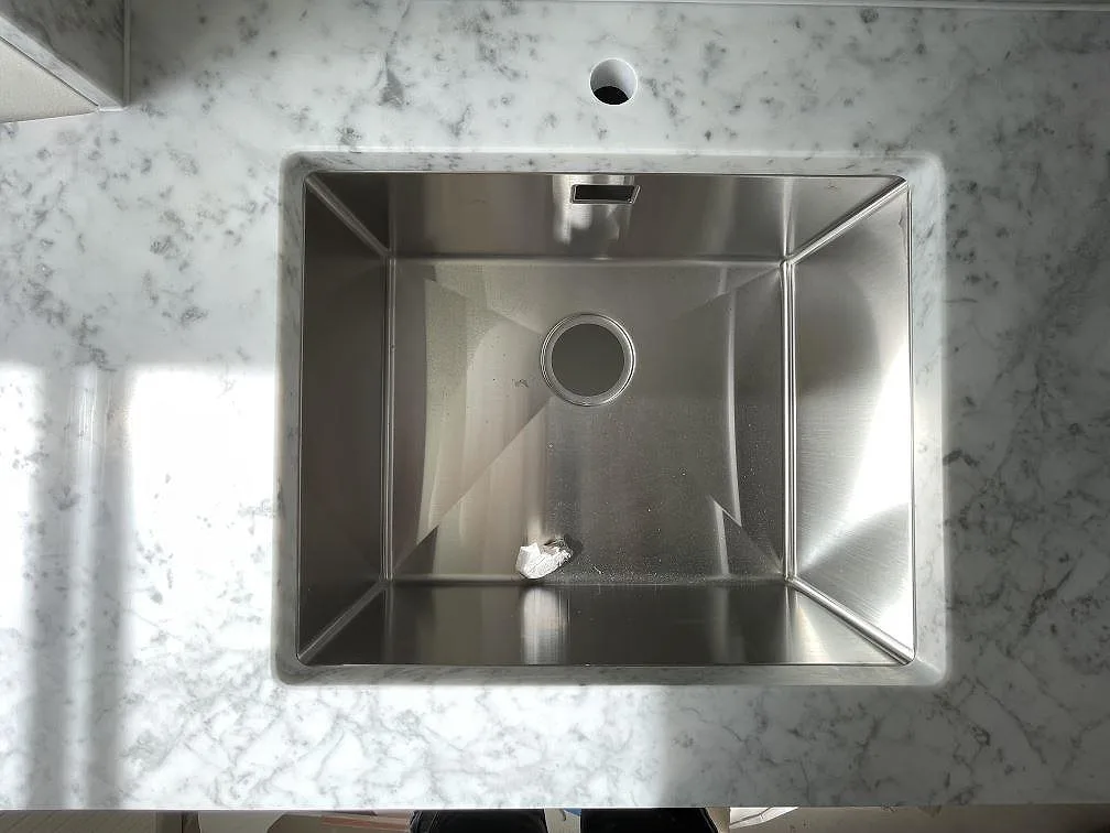 Underlimmad rostfri diskho infälld i en köksbänkskiva i vit Carrara C-marmor med grå ådring i Stockholm.