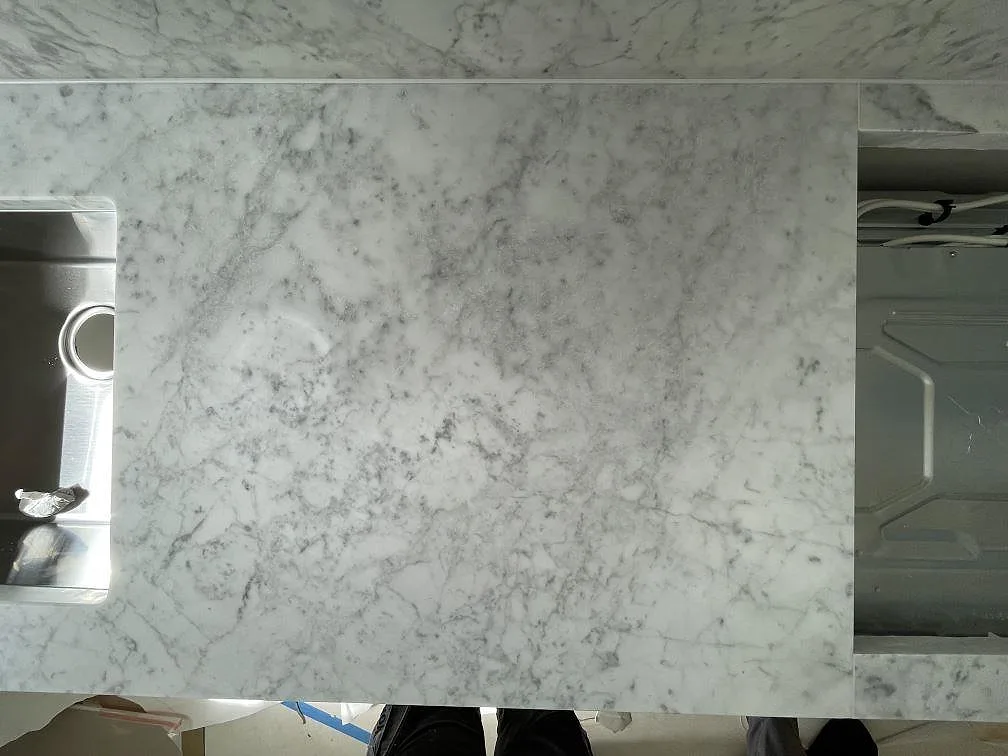 Bänkskiva i Carrara C-marmor med tydlig grå ådring och urtag för diskho och häll i ett kök under montering i Stockholm.