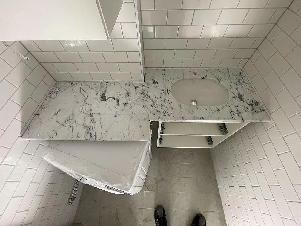 Badrum med tvättställsbänk i Carrara C-marmor och underlimmat keramiktvättställ mot vitt kakel i Stockholm.