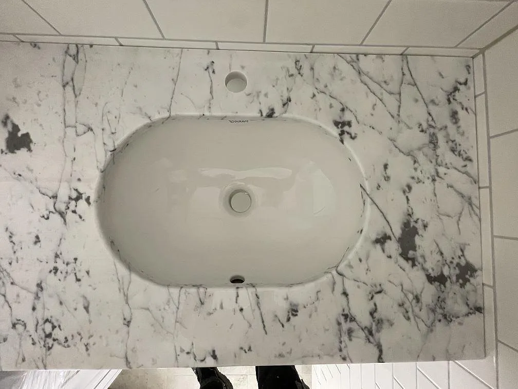 Underlimmat vitt Duravit-tvättställ i en marmorbänk i Carrara C med kraftig grå ådring i ett badrum i Stockholm.