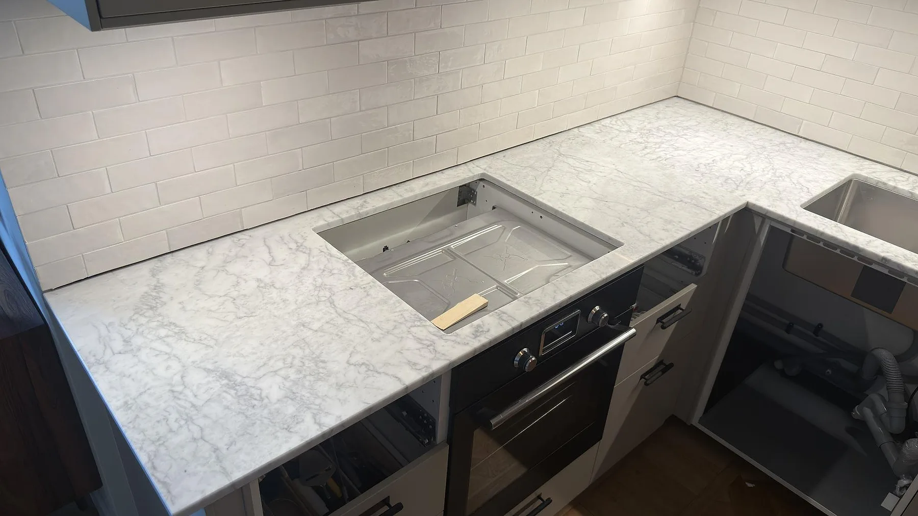Köksbänkskiva i vit Carrara C-marmor med matt finish och urtagning för häll mot vitt tegelkakel i ett kök i stockholm.