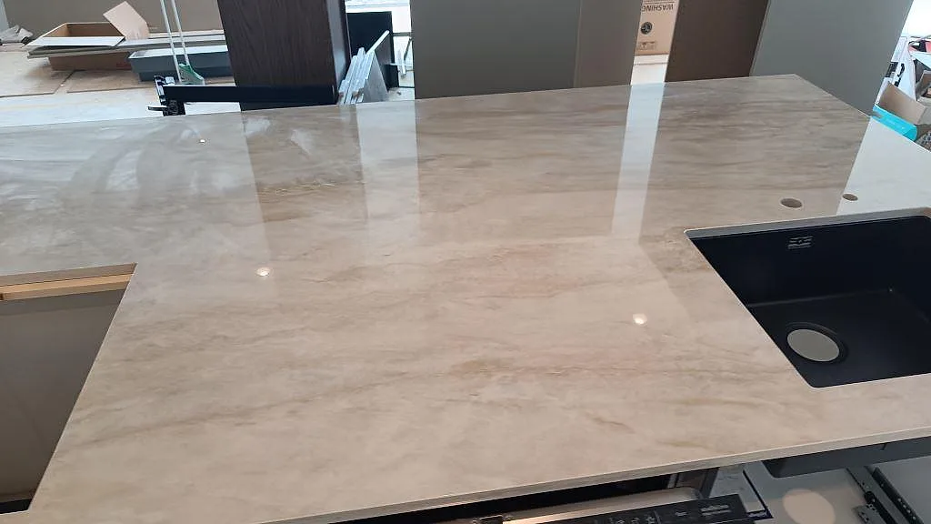 Polerad Carrara C bänkskiva med svart diskho och rund blandarhåltagning under köksmontering i Stora Höga.