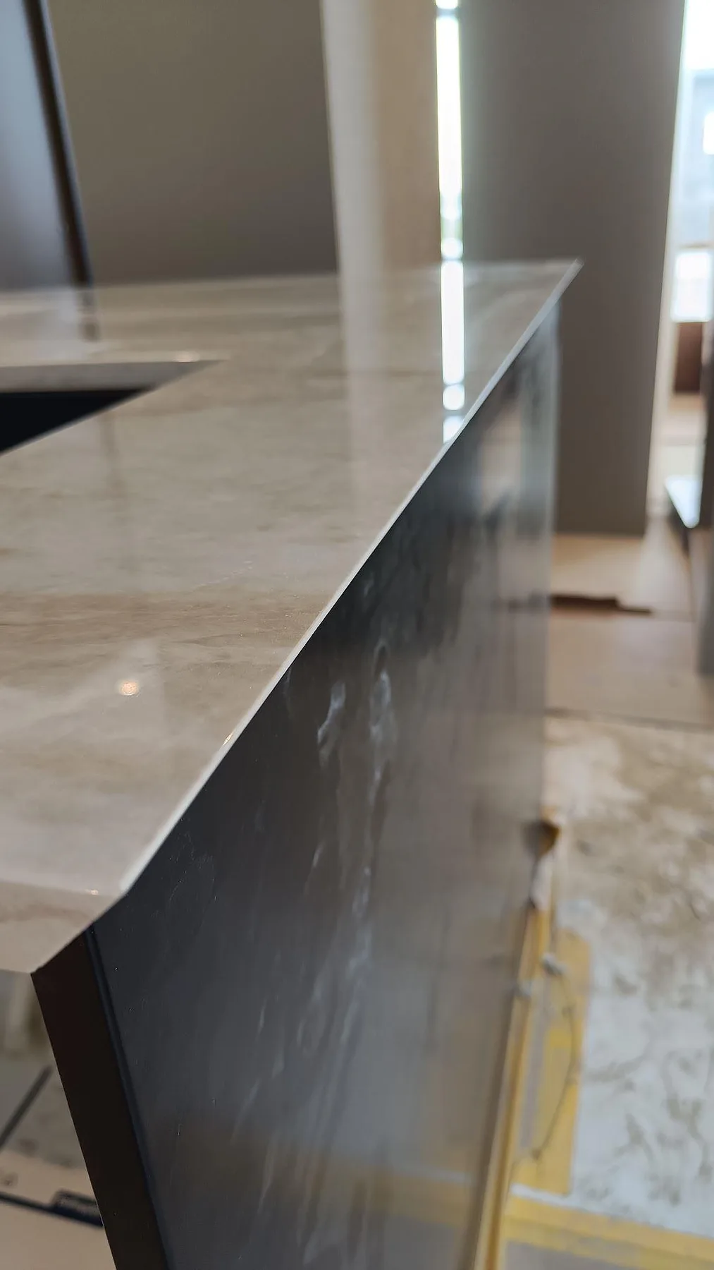 Smal detaljbild av vattenfallsida och polerad Carrara C bänkskiva med svart underlimmad diskho i Stora Höga.
