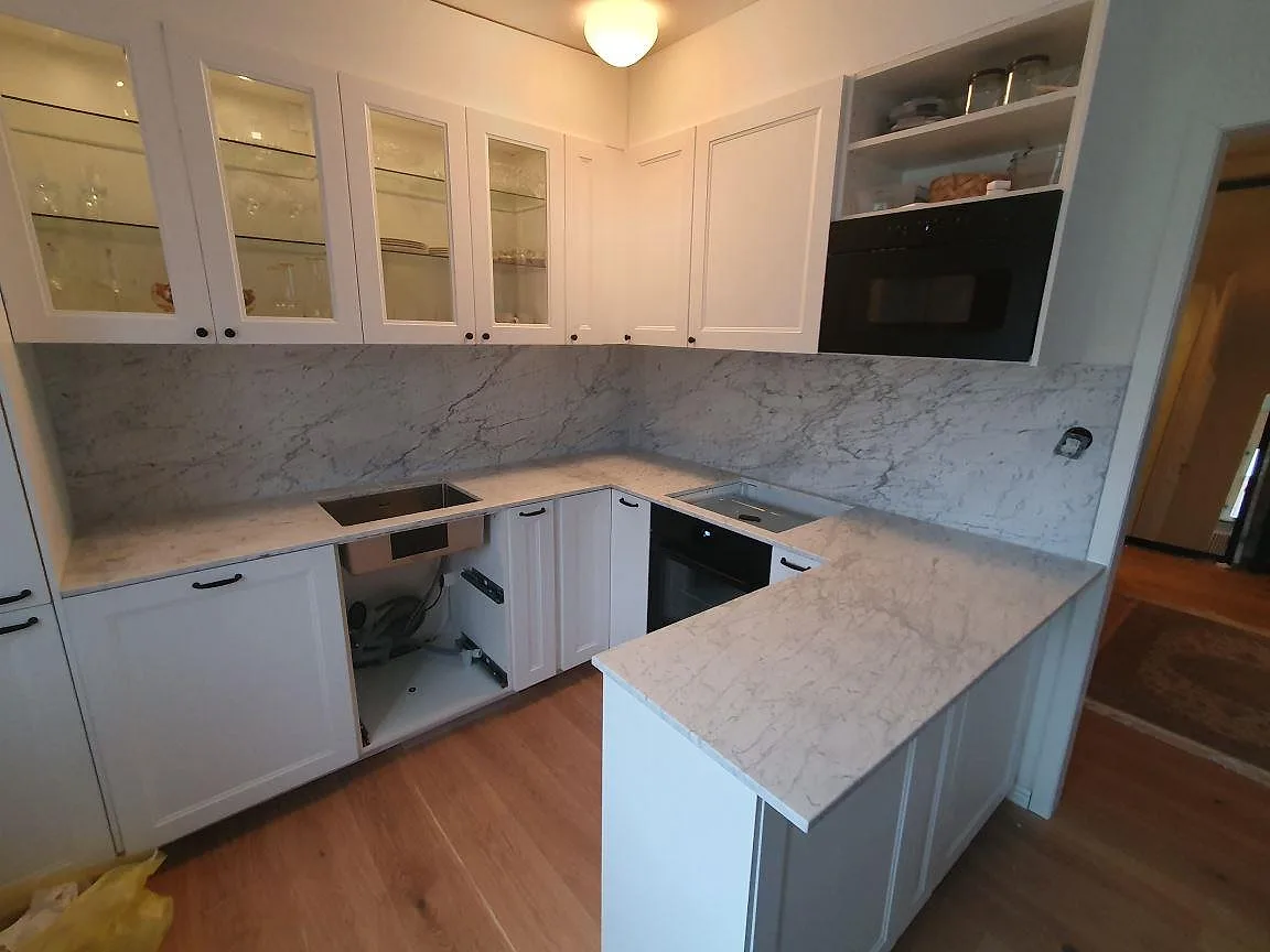 Köksbänkskiva i vit Carrara C-marmor, matt, med halvö och heltäckande stänkskydd i samma marmor i ett kök i Sundbyberg.