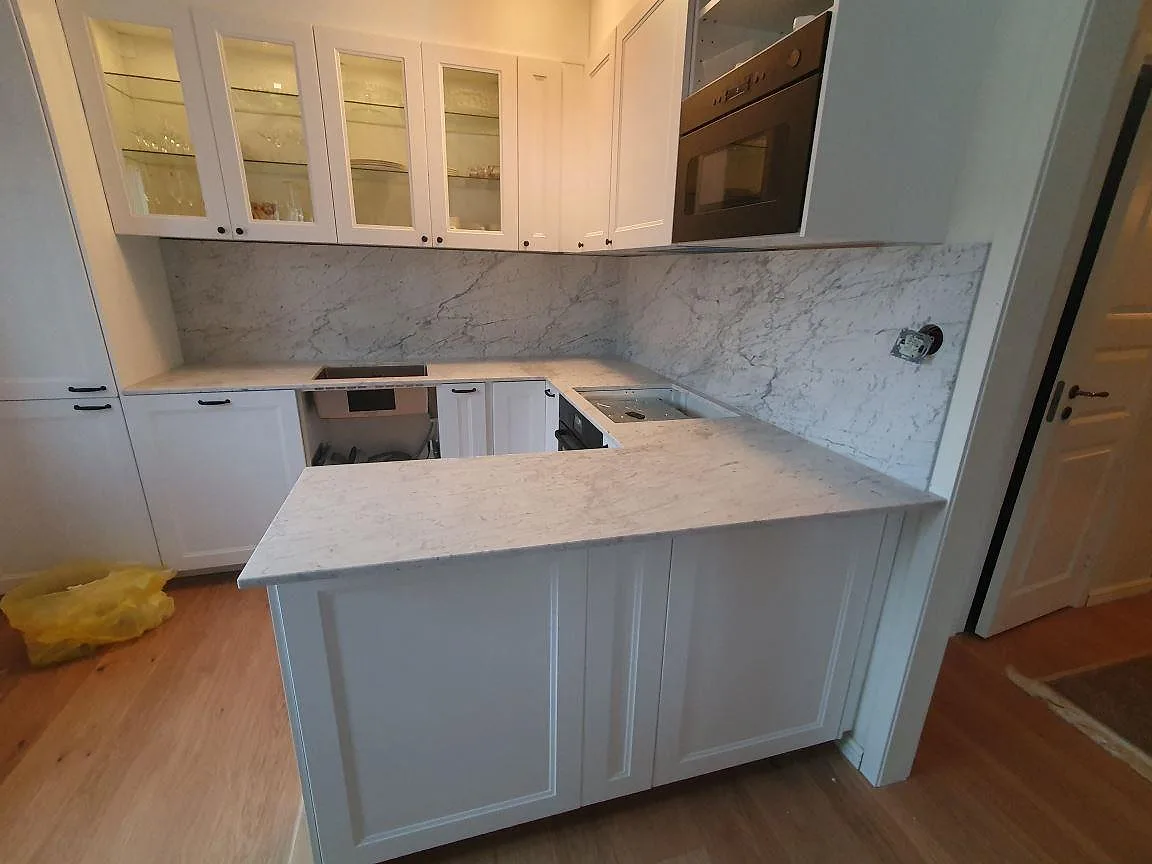 Matt Carrara C-marmorbänkskiva med tydlig grå ådring och underlimmad rostfri diskho i ett kök under montering i Sundbyberg.