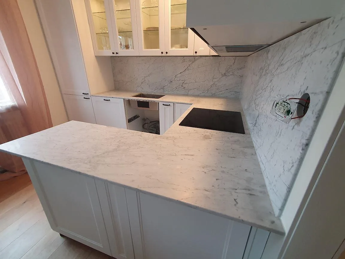 Carrara C-marmor på bänkskiva, halvö och stänkskydd med plats för induktionshäll i ett kök i Sundbyberg.