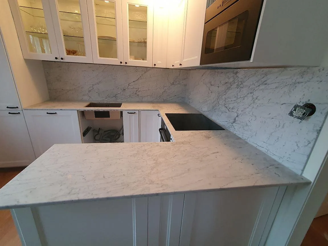 Köksbänkskiva och halvö i Carrara C-marmor med induktionshäll och matt yta i ett kök i Sundbyberg.