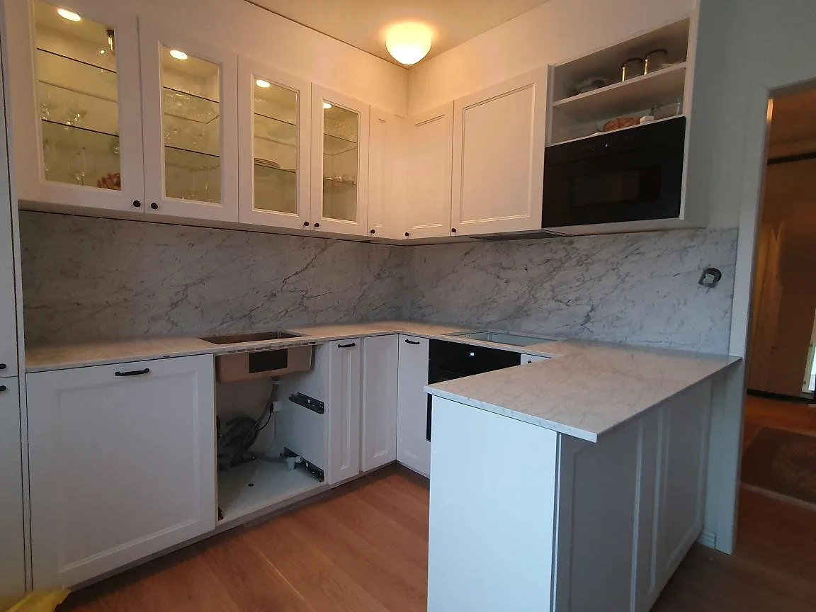 Vinkelkök med matt Carrara C-marmor på bänkskiva och stänkskydd, underlimmad rostfri diskho och marmorhalvö i Sundbyberg.