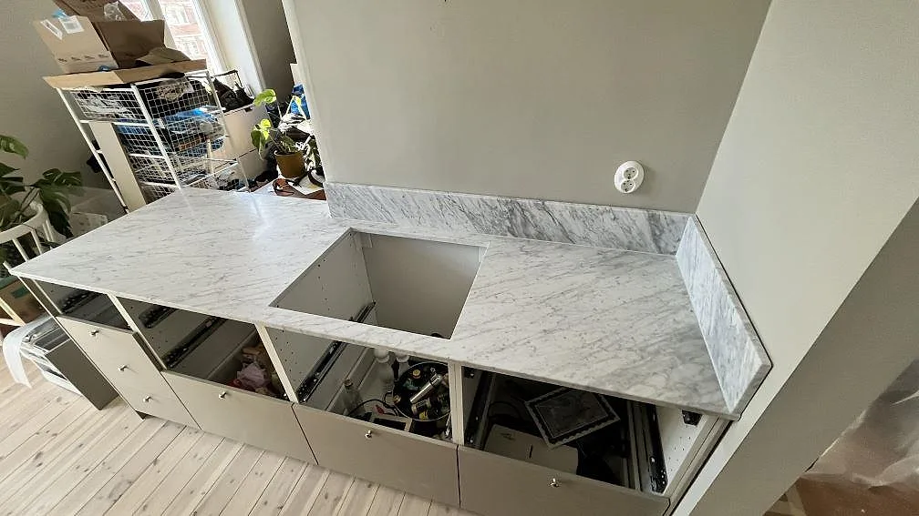 Matt Carrara C marmor som köksbänkskiva med rektangulärt urtag och uppvikt stänkkant under montering i Sundbyberg.