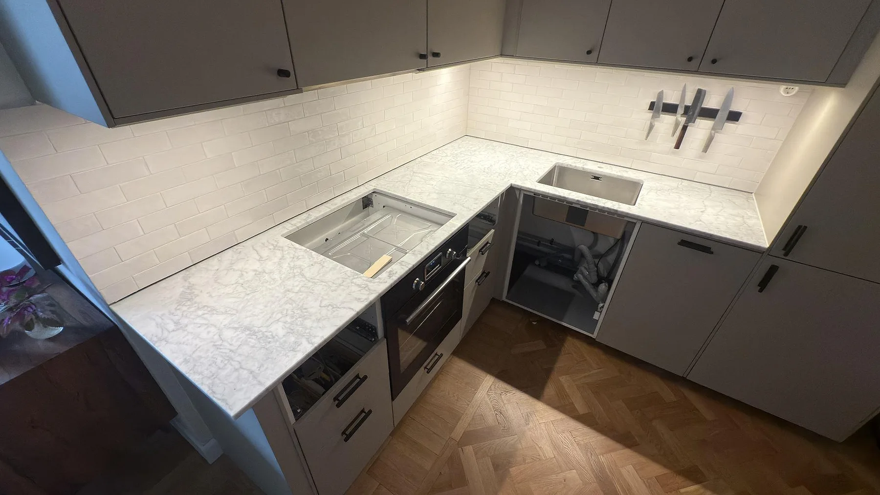 L-format kök med polerad köksbänkskiva i Carrara C marmor, underlimmad rostfri diskho och hällurtag under montering.