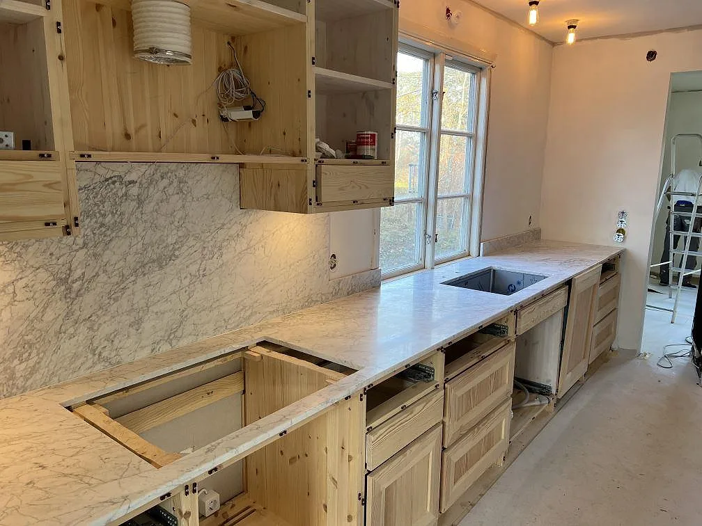 Matt köksbänkskiva i Carrara C marmor med tydlig ådring, stänkskydd och urtag i ett kök under montering i Täby.