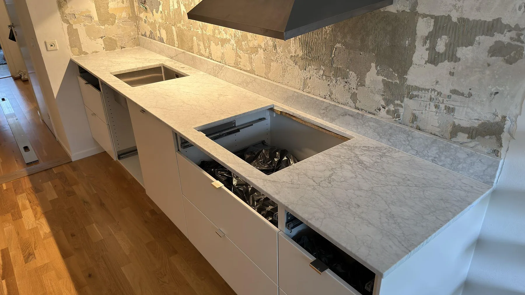 Köksbänkskiva i matt Carrara C marmor med synlig ådring, låg stänkkant och öppningar för diskho och häll under montering i Täby.