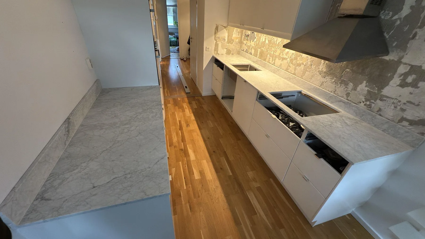 Matt köksbänkskiva i Carrara C marmor med låg stänkkant, öppningar för diskho och häll samt separat arbetsyta i ett smalt kök i Täby.