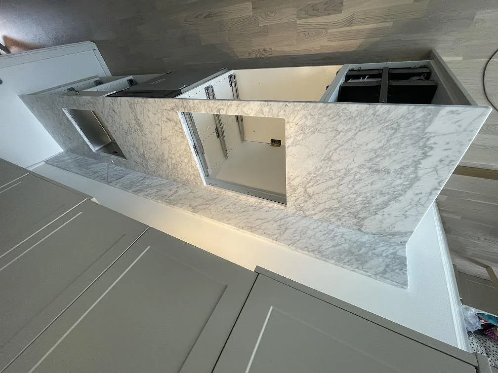 Köksbänkskiva i matt Carrara C-marmor med underlimmad rostfri diskho och förberedd hällöppning i ett kök i Täby.