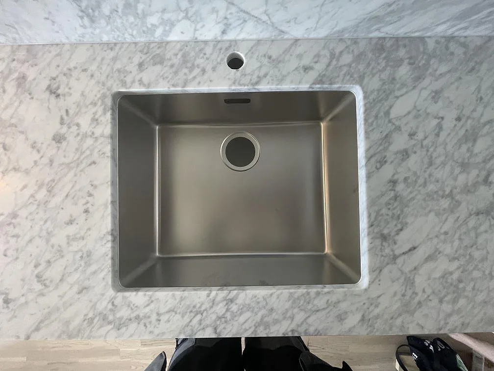 Närbild på underlimmad rostfri diskho i matt Carrara C-marmor med blandarhål och grå ådring i Täby.