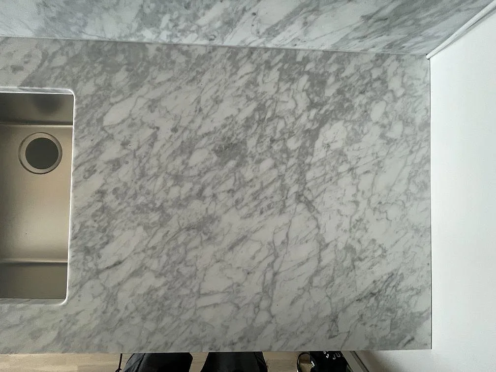 Detalj av matt Carrara C-marmor vid en underlimmad rostfri diskho, med tydlig grå ådring i ett kök i Täby.