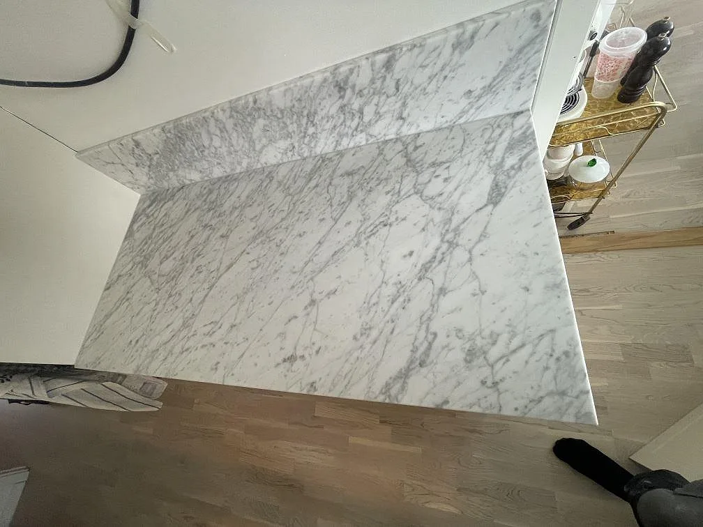 Top-down-vy av matt köksbänkskiva i Carrara C-marmor med uppkant och ljusa köksstommar i Täby.