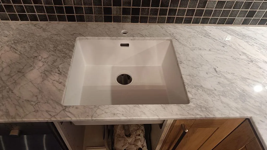 Underlimmad diskho i polerad Carrara C marmor med grå ådring och mörkt mosaikstänkskydd i kök i Timmersdala.