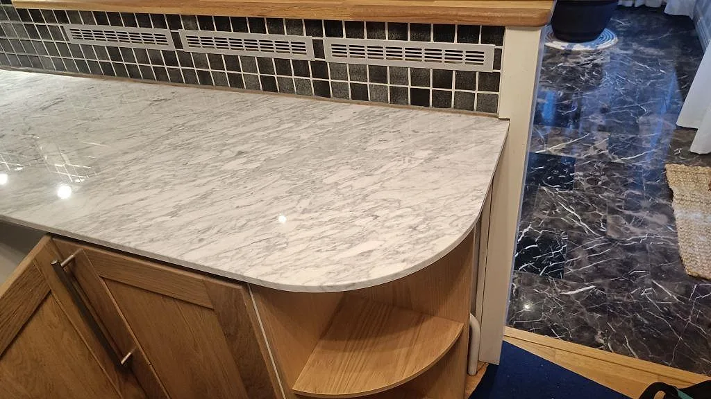Rundat avslut på köksö i polerad Carrara C marmor med träinredning och grå ådring i Timmersdala.