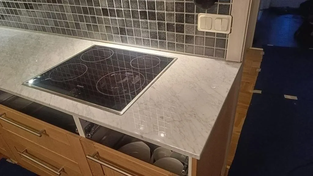 Induktionshäll infälld i polerad Carrara C köksbänkskiva med mörkt mosaikkakel i Timmersdala.