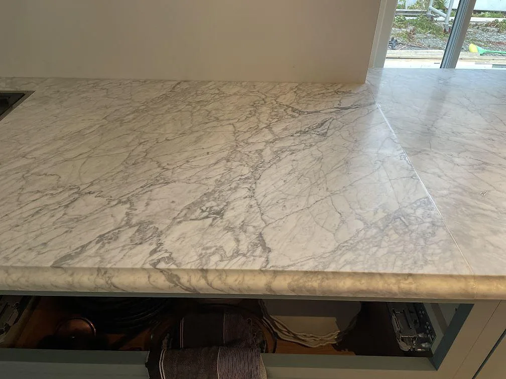 Närbild av ådrad Carrara C marmorskiva, matt, som arbetsyta över öppna skåpstommar i Tisvilde.
