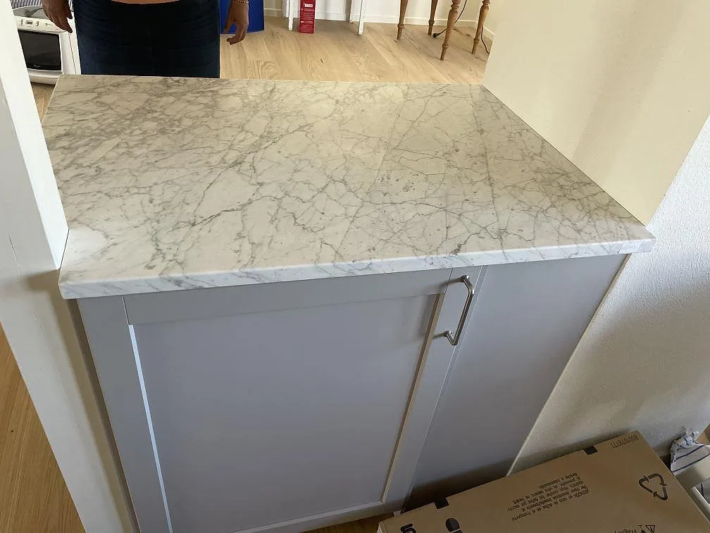 Närbild på matt Carrara C marmorskiva över vita köksstommar i ett kök under montering i Torekov.