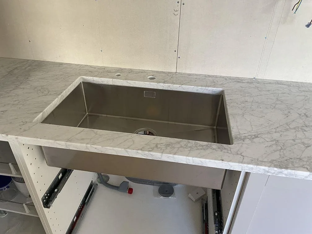Rostfri underlimmad diskho i matt Carrara C marmor med öppna köksstommar under montering i Torekov.