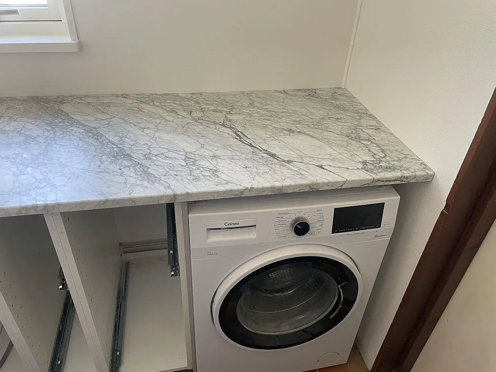 Tvättdel med bänkskiva i matt Carrara C marmor över tvättmaskin i Torekov.