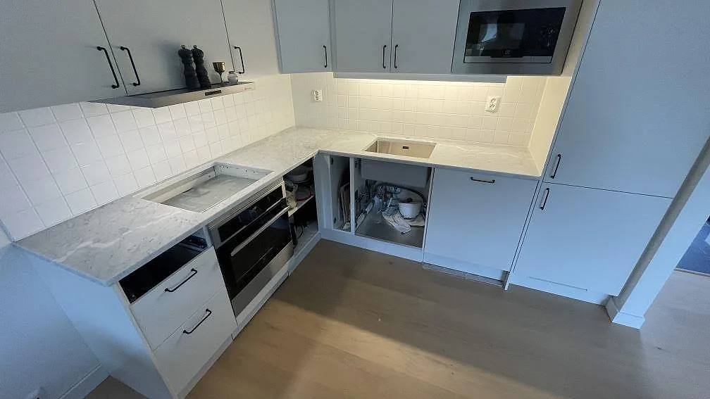 L-formad köksbänkskiva i matt Carrara C-marmor i ett kök i Torekov, med rostfri diskho och plats för häll.