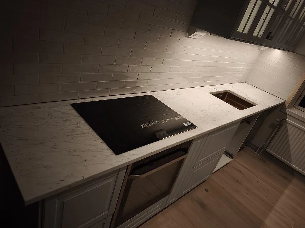 Köksbänkskiva i matt Carrara C marmor med svart häll och rostfri diskho i ett kök i Torekov.