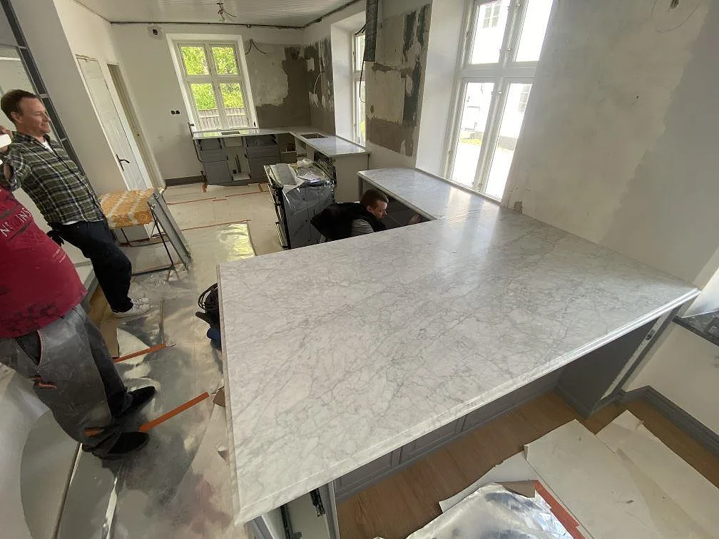 Köksbänkskiva i vit Carrara C-marmor, matt, med stor U-formad köksbänk under montering i ett kök i Trelleborg.