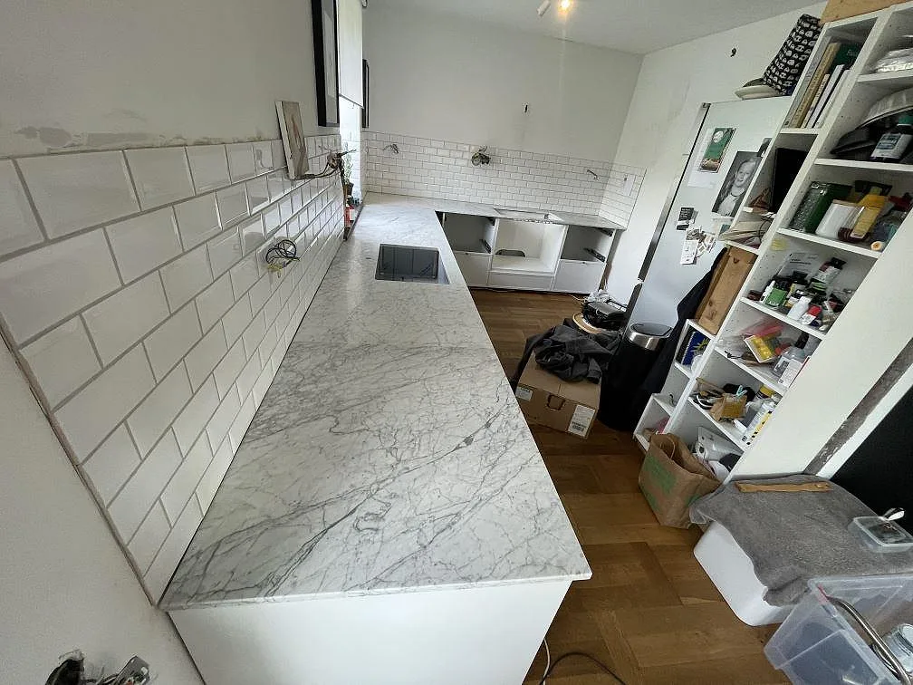 L-formad köksbänkskiva i Carrara C marmor, matt, med häll och vitt subway-kakel i ett kök i Trelleborg.
