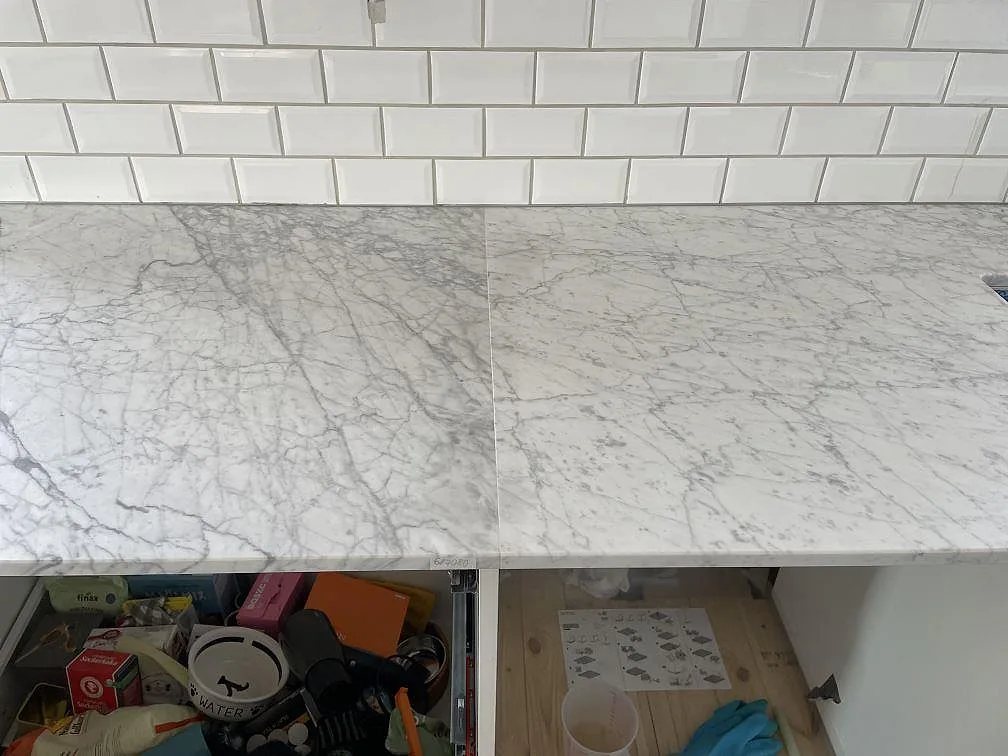 Skarv och ådring i matt Carrara C marmor på installerad köksbänkskiva framför vitt kakel i Trelleborg.