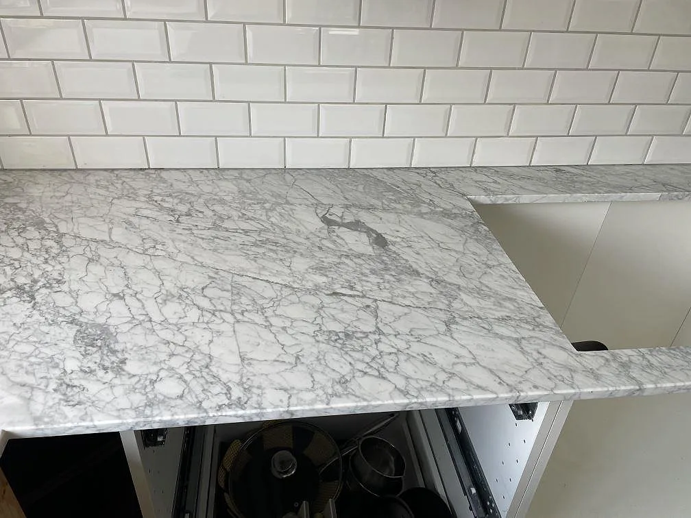 Närbild på Carrara C marmorbänkskiva, matt, med diskhoöppning och vitt kakel i ett kök i Trelleborg.